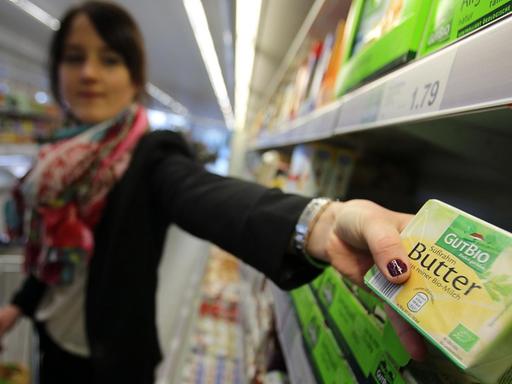 Eine Frau nimmt in einem Supermarkt Bio-Butter aus dem Regal.