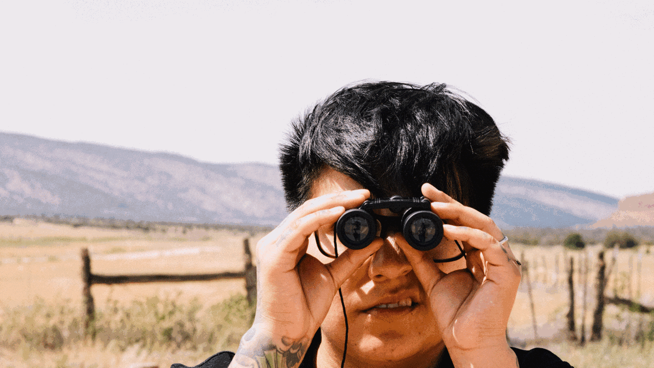 Serie Observateur - Ein junger Mann schaut mit einem Fernglas in die Kamera.