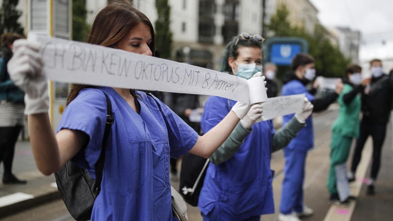 Eine medizinische Pflegekraft, in blauer Krankenhaus-Bekleding, hält während einer Demonstration ein Stück Toilettenpapier mit der Aufschrift "Ich bin kein Oktopus mit 8 Armen" in den Händen. Eine medizinische Pflegekraft, in blauer Krankenhaus-Bekleding, hält während einer Demonstration ein Stück Toilettenpapier mit der Aufschrift "Ich bin kein Oktopus mit 8 Armen" in den Händen.