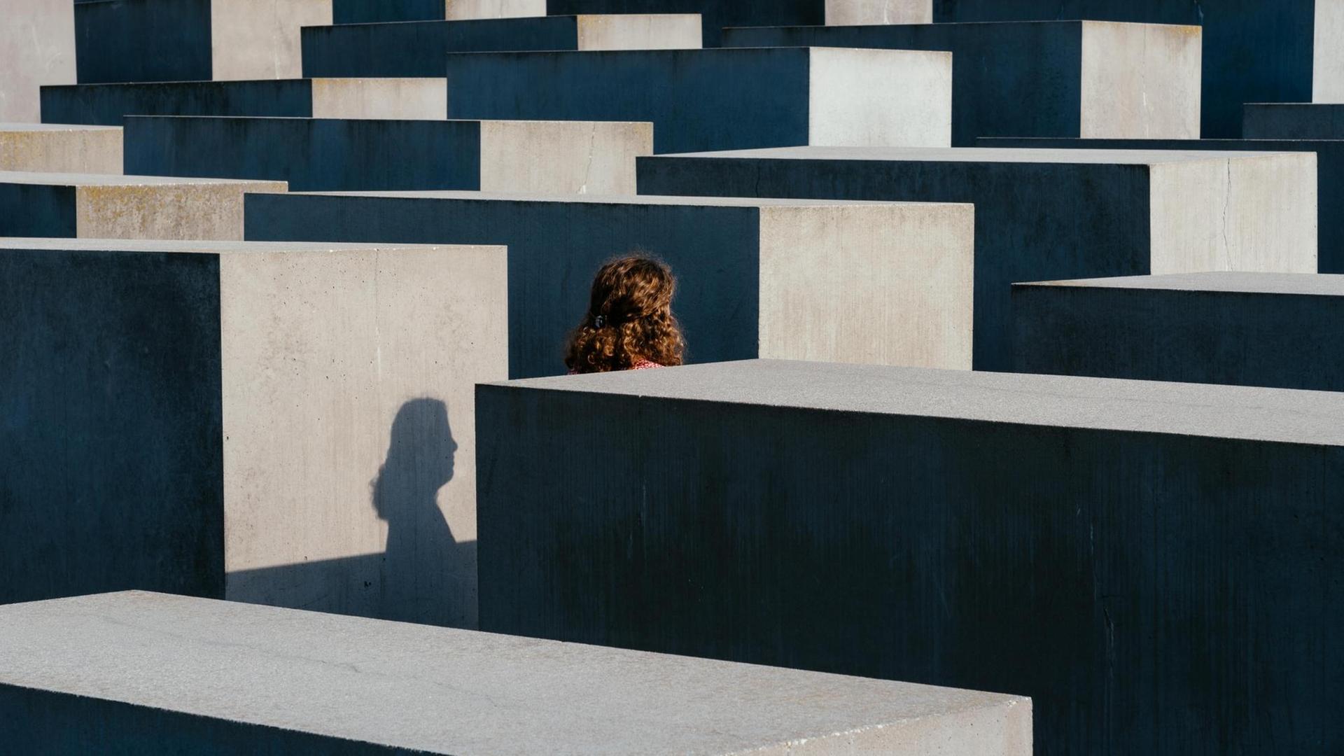 Blick auf die Säulen des Mahnmals. Dazwischen läuft eine Frau deren Profil sich als Schatten auf einer der Säulen abbildet. Blick auf die Säulen des Mahnmals. Dazwischen läuft eine Frau deren Profil sich als Schatten auf einer der Säulen abbildet.