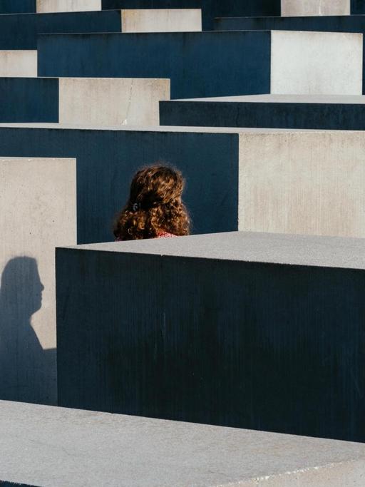 Blick auf die Säulen des Mahnmals. Dazwischen läuft eine Frau deren Profil sich als Schatten auf einer der Säulen abbildet.
