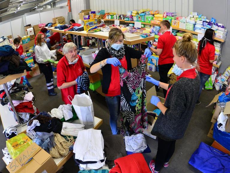 Man sieht eine Halle mit Regalen voller Kleidung und Helfer, die Kleidungsstücke sortieren.