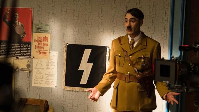 Taika Waititi steht in Nazi-Uniform und mit Hitlerbärtchen in einem Filmset.
