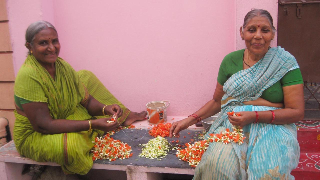Und fertig ist der Blütenkranz: Zwei Frauen in einem Hof vor ihrem Haus in Südindien.