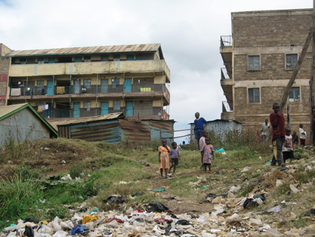 Kinder stehen vor zwei Gebäuden im Slumviertel Korogocho in Nairobi, Kenia, welches direkt an die Mülldeponie Dandora grenzt.