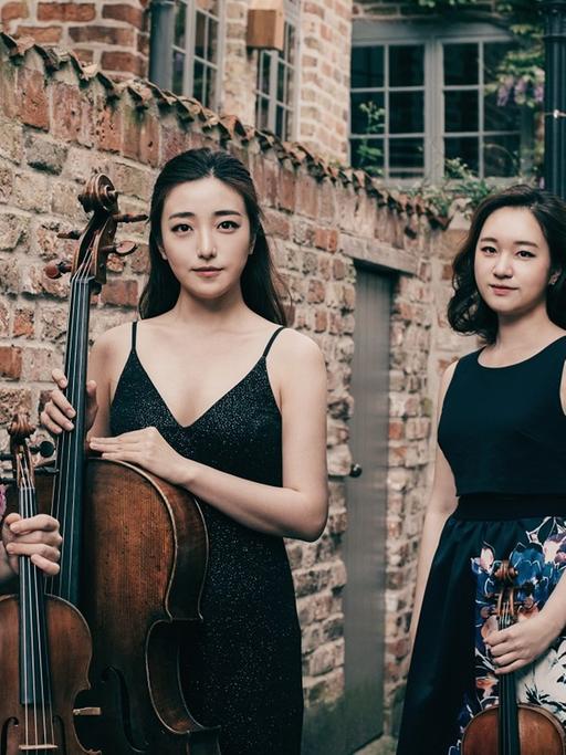 Die vier Musikerinnen stehen in blumenbedruckten schwarzen Konzertkleidern vor einer Ziegelmauer