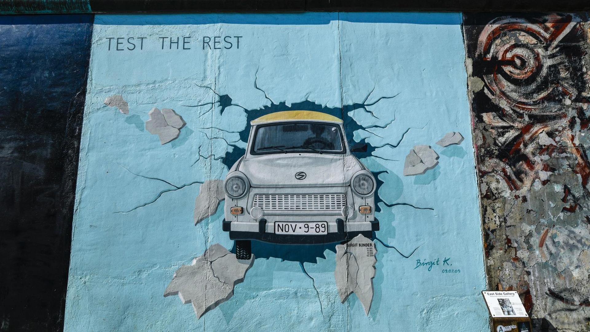 Eine der Abbildungen an der East Side Gallery in Berlin zeigt einen hellblauen Trabi, der durch eine Wand stößt. Eine der Abbildungen an der East Side Gallery in Berlin zeigt einen hellblauen Trabi, der durch eine Wand stößt.