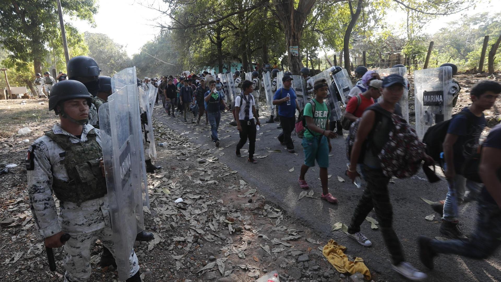 Mitglieder der mexikanischen Nationalgarde halten Migranten auf. Die Uniformierten tragen durchsichtige Schutzschilder.