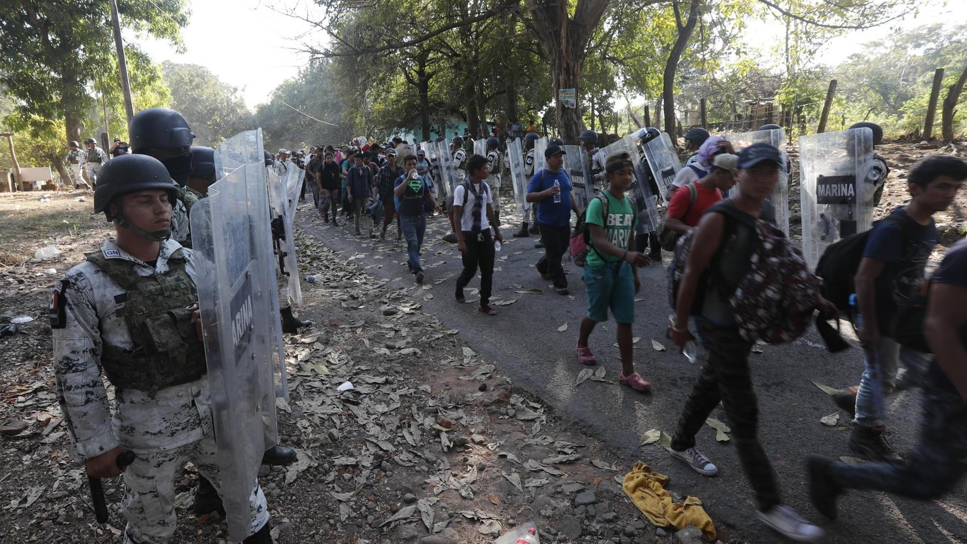 Mitglieder der mexikanischen Nationalgarde halten Migranten auf. Die Uniformierten tragen durchsichtige Schutzschilder. Mitglieder der mexikanischen Nationalgarde halten Migranten auf. Die Uniformierten tragen durchsichtige Schutzschilder.
