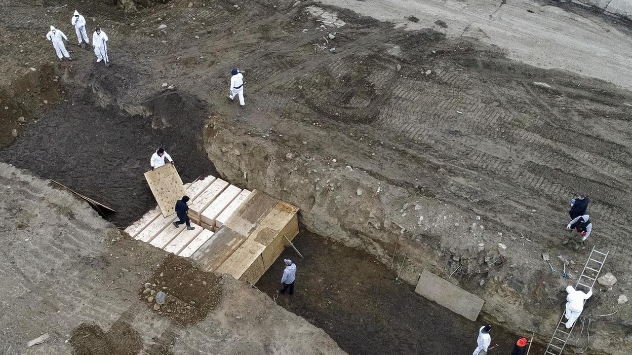 Arbeiter in Schutzanzügen vergraben einfache Holzsärge in einem Graben auf Hart Island in der New Yorker Bronx. Der Landstreifen auf der kleinen Insel soll als Lösung für vorübergehende Begräbnisse für Corona-Tote dienen.