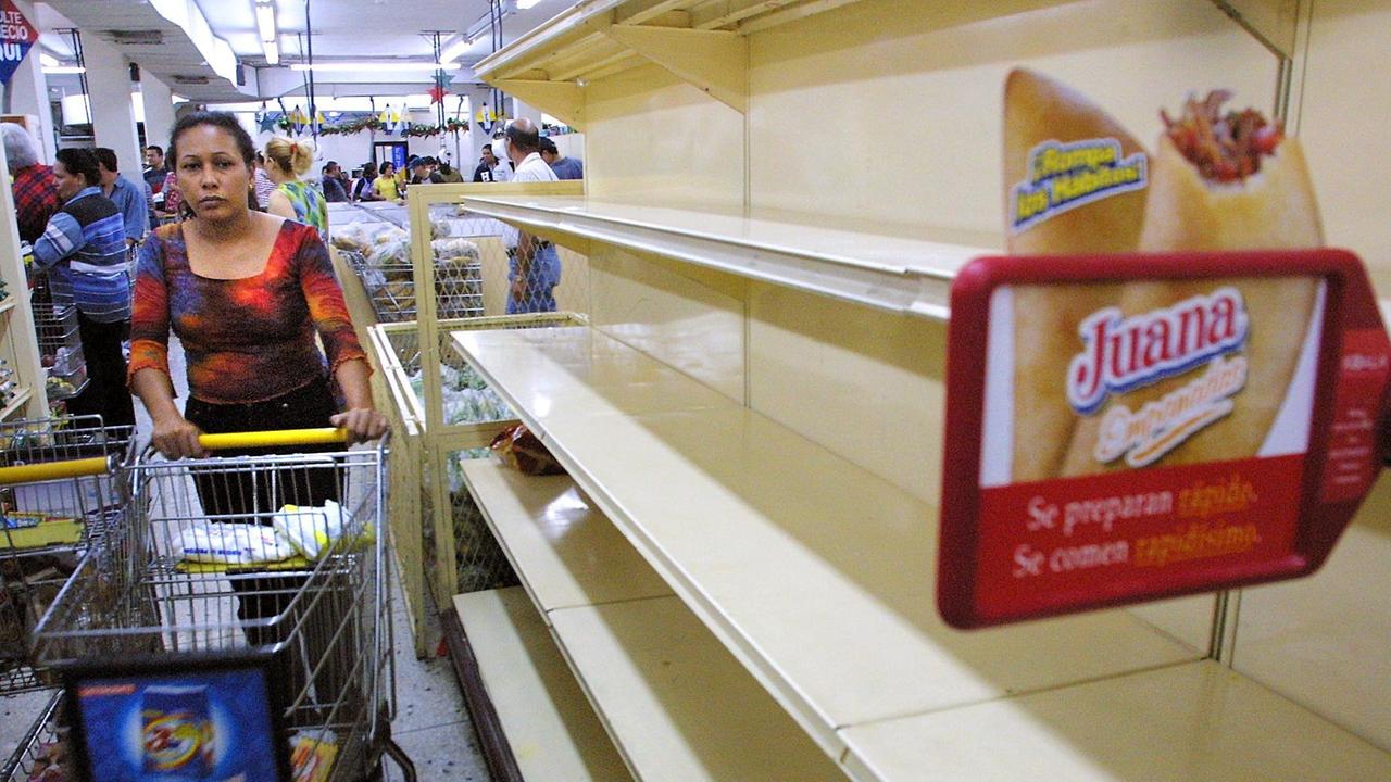 Eine Frau fährt mit einem Einkaufswagen an leeren Regalen in einem Supermarkt in Maracaibo in Venezuela Eine Frau fährt mit einem Einkaufswagen an leeren Regalen in einem Supermarkt in Maracaibo in Venezuela
