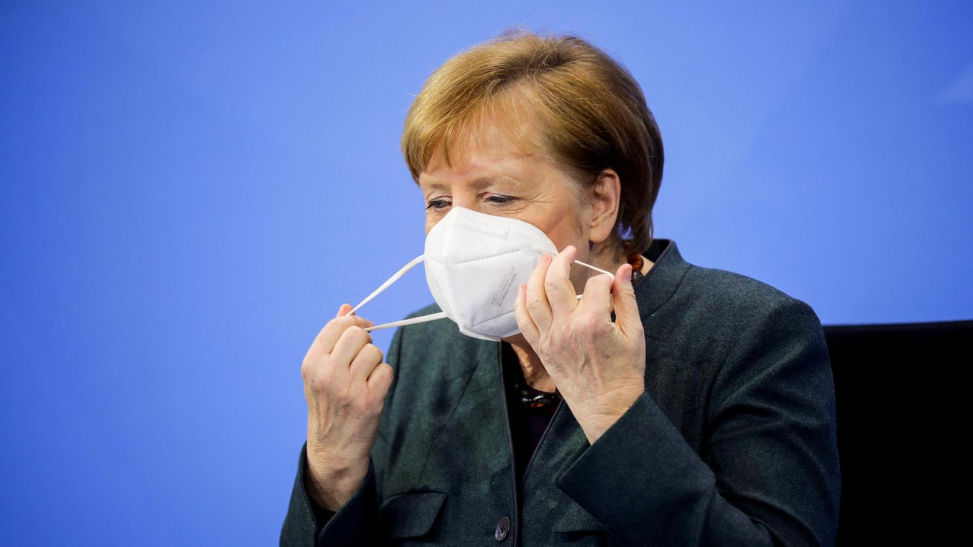 Bundeskanzlerin Angela Merkel (CDU) zieht sich vor Beginn der Pressekonferenz im Bundeskanzleramt über die Ergebnisse der Bund-Länder-Beratungen die Maske ab. Der bis Ende Januar befristete Lockdown zur Eindämmung der Corona-Pandemie in Deutschland wird bis Mitte Februar verlängert.