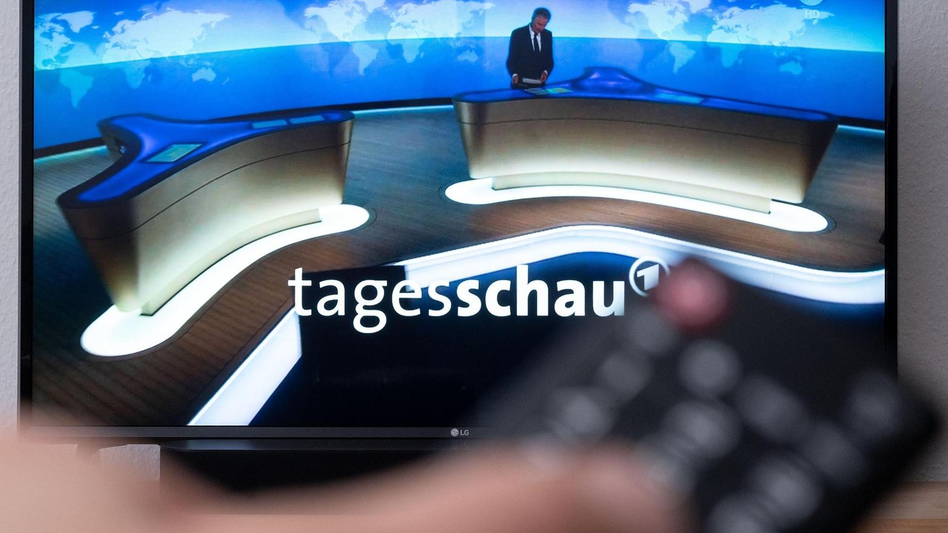 Ein Mann hält eine Fernbedienung vor einen Fernseher, auf dem die Tagesschau läuft. Ein Mann hält eine Fernbedienung vor einen Fernseher, auf dem die Tagesschau läuft.