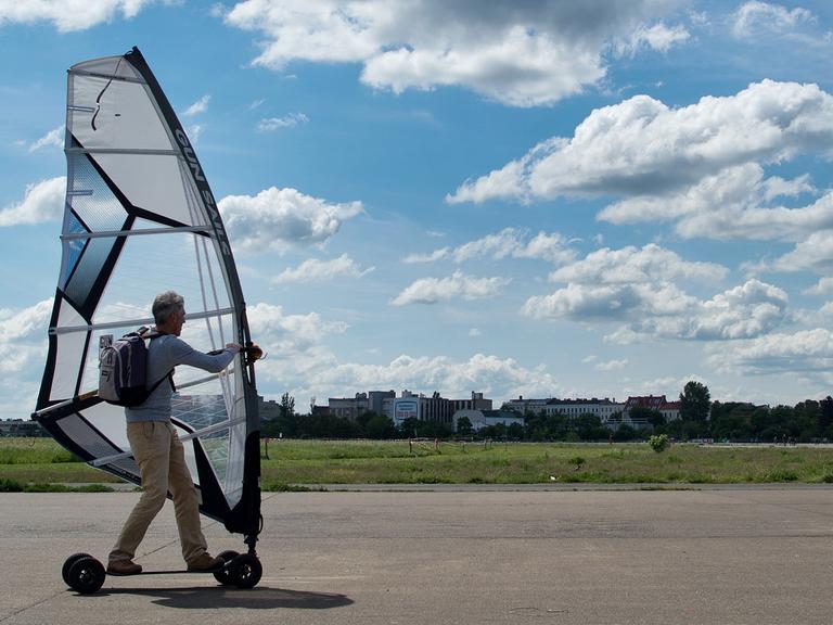 Auf dem alten Flughafen Tempelhof ist auch viel Platz für Sportler. Hier sehen wir einen Wind-Surfer auf einem Brett mit Rollen und Segel.