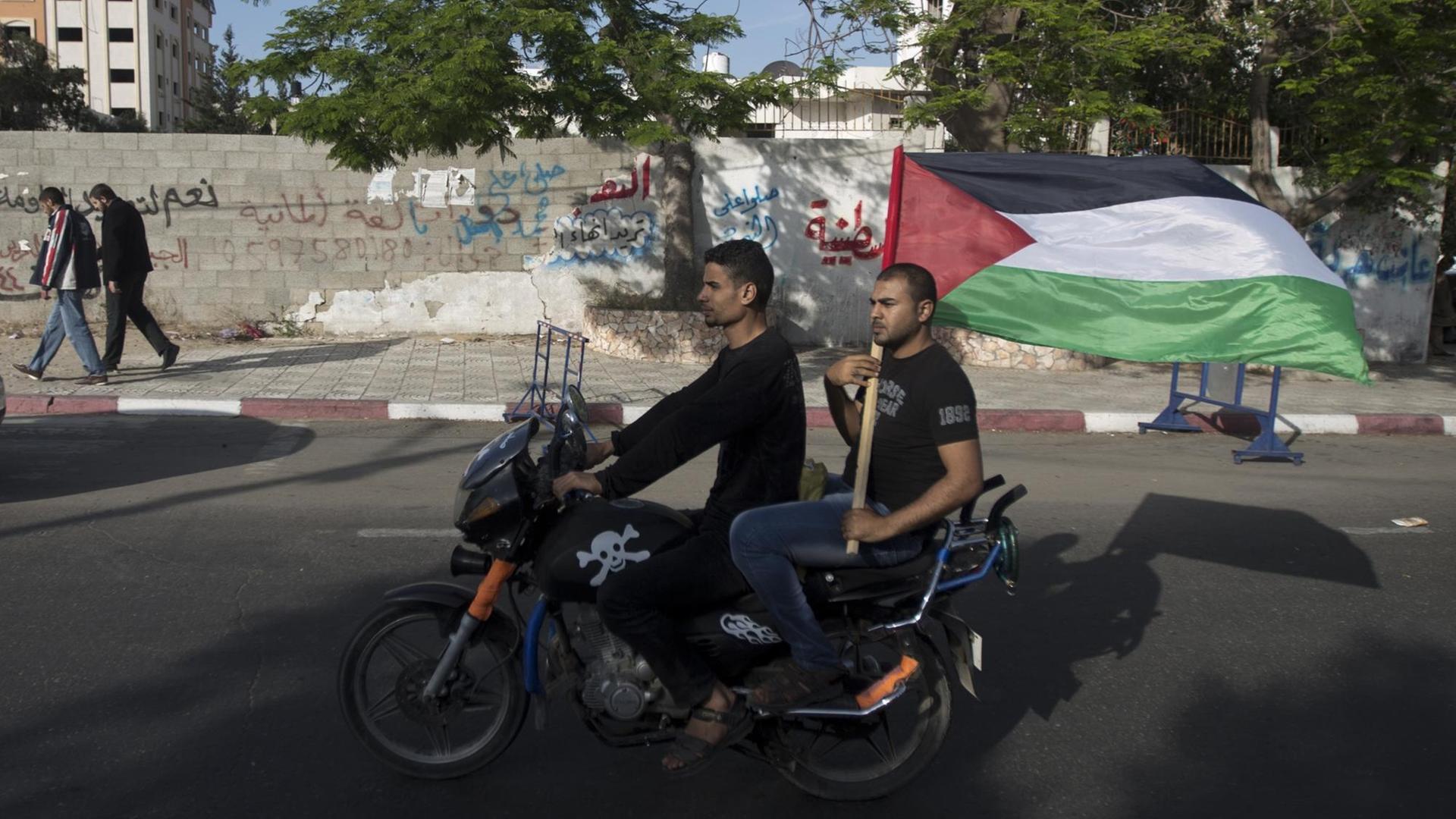 Zwei Palästinenser in Gaza-City fahren auf einem Motorrad, einer hält die palästinensische Flagge in die Luft. Zwei Palästinenser in Gaza-City fahren auf einem Motorrad, einer hält die palästinensische Flagge in die Luft.
