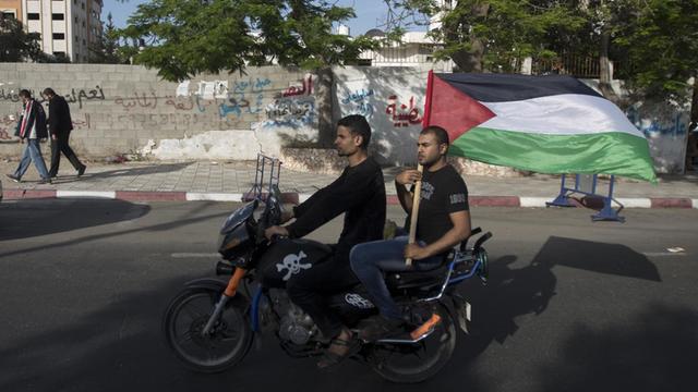 Zwei Palästinenser in Gaza-City fahren auf einem Motorrad, einer hält die palästinensische Flagge in die Luft.