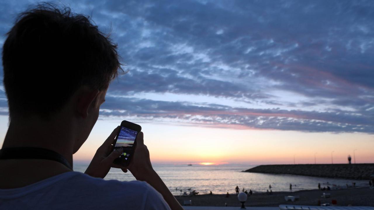 Ein Touristen macht ein Foto vom Sonnenuntergang.