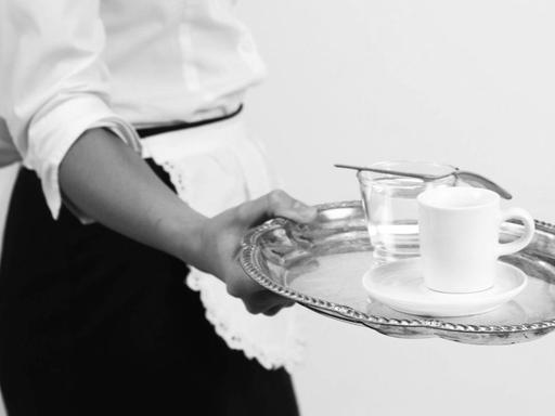 Eine Kellnerin in einer weissen Schürze serviert Espresso auf einem Silbertablett.