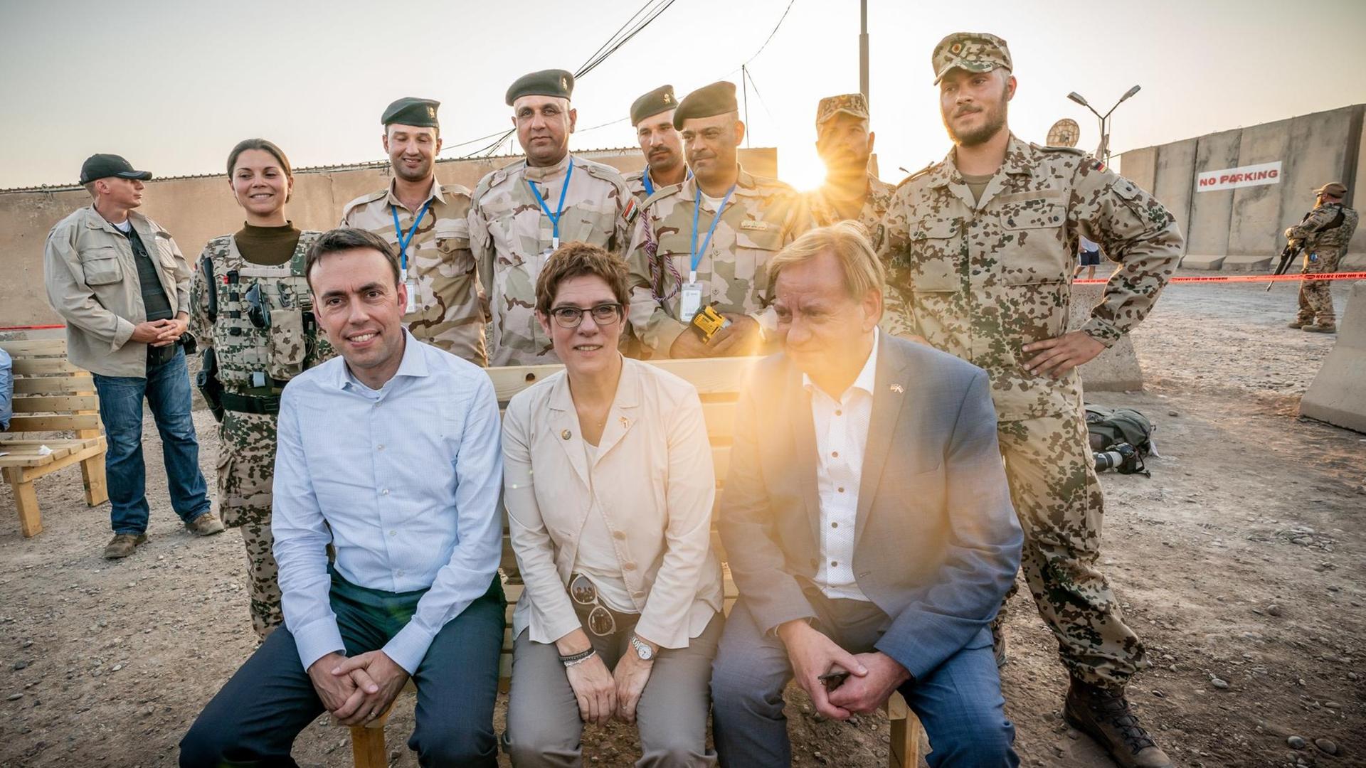 20.08.2019, Irak, Bagdad: Annegret Kramp-Karrenbauer (CDU), Verteidigungsministerin, sitzt beim Besuch der Bundeswehrsoldaten im internationalen Militärlager Camp Taji zwischen den Bundestagsabgeordneten Ingo Gädechens (CDU, vorne rechts) und Nils Schmid (SPD, vorne links) auf einer Bank, die Pioniere zuvor mit Irakischen Soldaten gezimmert hatten. Die Ministerin und CDU-Chefin führt politische Gespräche in der Hauptstadt Bagdad und trifft deutsche Soldaten, die an der Ausbildung einheimischer Kräfte in dem Land beteiligt sind. Foto: Michael Kappeler/dpa | Verwendung weltweit 20.08.2019, Irak, Bagdad: Annegret Kramp-Karrenbauer (CDU), Verteidigungsministerin, sitzt beim Besuch der Bundeswehrsoldaten im internationalen Militärlager Camp Taji zwischen den Bundestagsabgeordneten Ingo Gädechens (CDU, vorne rechts) und Nils Schmid (SPD, vorne links) auf einer Bank, die Pioniere zuvor mit Irakischen Soldaten gezimmert hatten. Die Ministerin und CDU-Chefin führt politische Gespräche in der Hauptstadt Bagdad und trifft deutsche Soldaten, die an der Ausbildung einheimischer Kräfte in dem Land beteiligt sind. Foto: Michael Kappeler/dpa | Verwendung weltweit