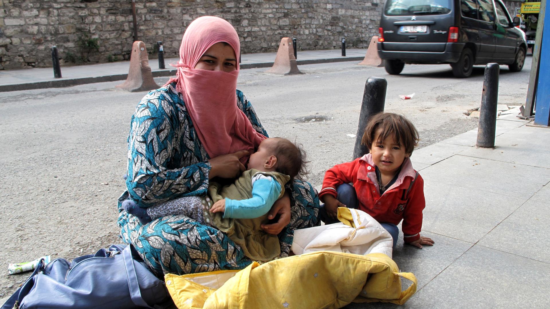 Die Syrerin Fatima mit ihren Kindern auf dem staubigen Bürgersteig einer Straße in Istanbul und bettelt, aufgenommen 2014.
