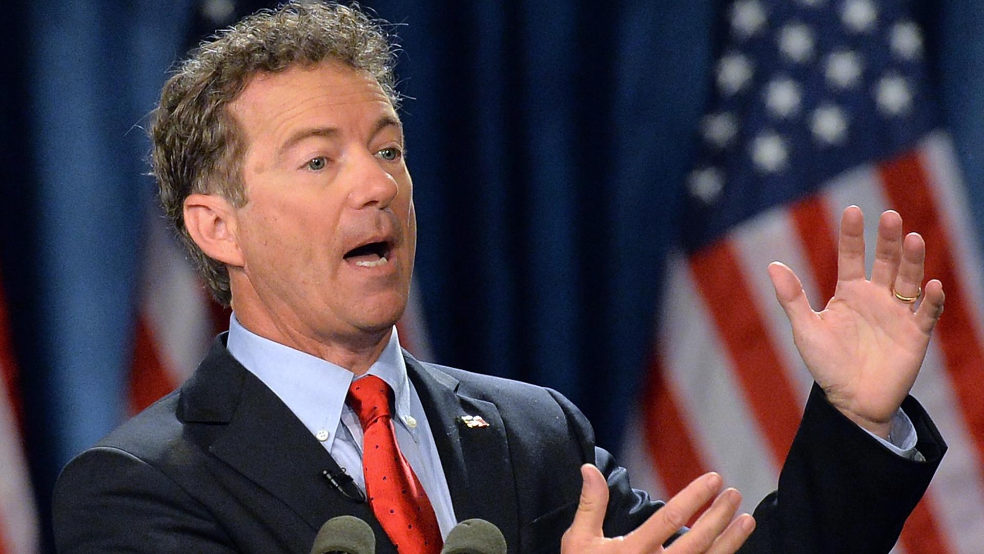 Rand Paul an einem Rednerpult sprechend und gestikulierend, im Hintergrund amerikanische Flaggen. Rand Paul an einem Rednerpult sprechend und gestikulierend, im Hintergrund amerikanische Flaggen.