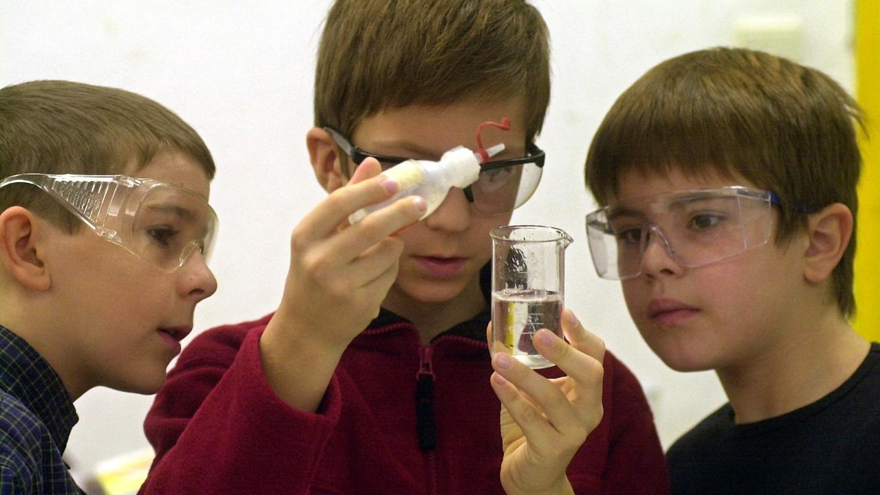 Ein achtjähriger Junge träufelt Kokosfett in ein Gefäß mit Leitungswasser, zwei andere Jungs schauen ihm dabei zu. Die Kinder tragen Schutzbrillen. Ein achtjähriger Junge träufelt Kokosfett in ein Gefäß mit Leitungswasser, zwei andere Jungs schauen ihm dabei zu. Die Kinder tragen Schutzbrillen.