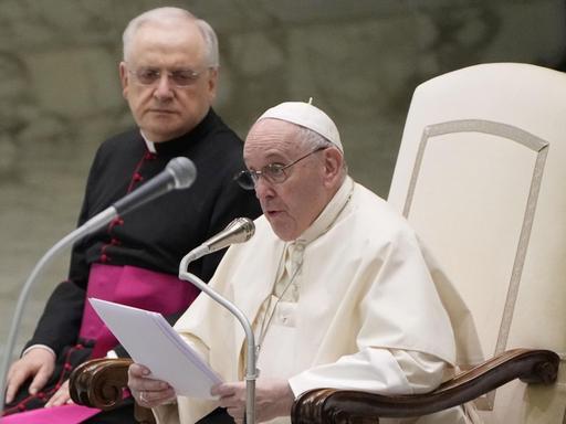 Papst Franziskus sitzt auf einem weißen Sessel in der Vatikanischen Audienzhalle
