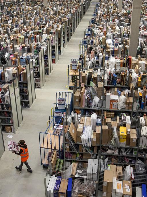 Eine Mitarbeiterin von Amazon läuft in einer der Lagerhallen des Amazon Logistikzentrums in Pforzheim an tausenden unverpackten Kartons vorbe.