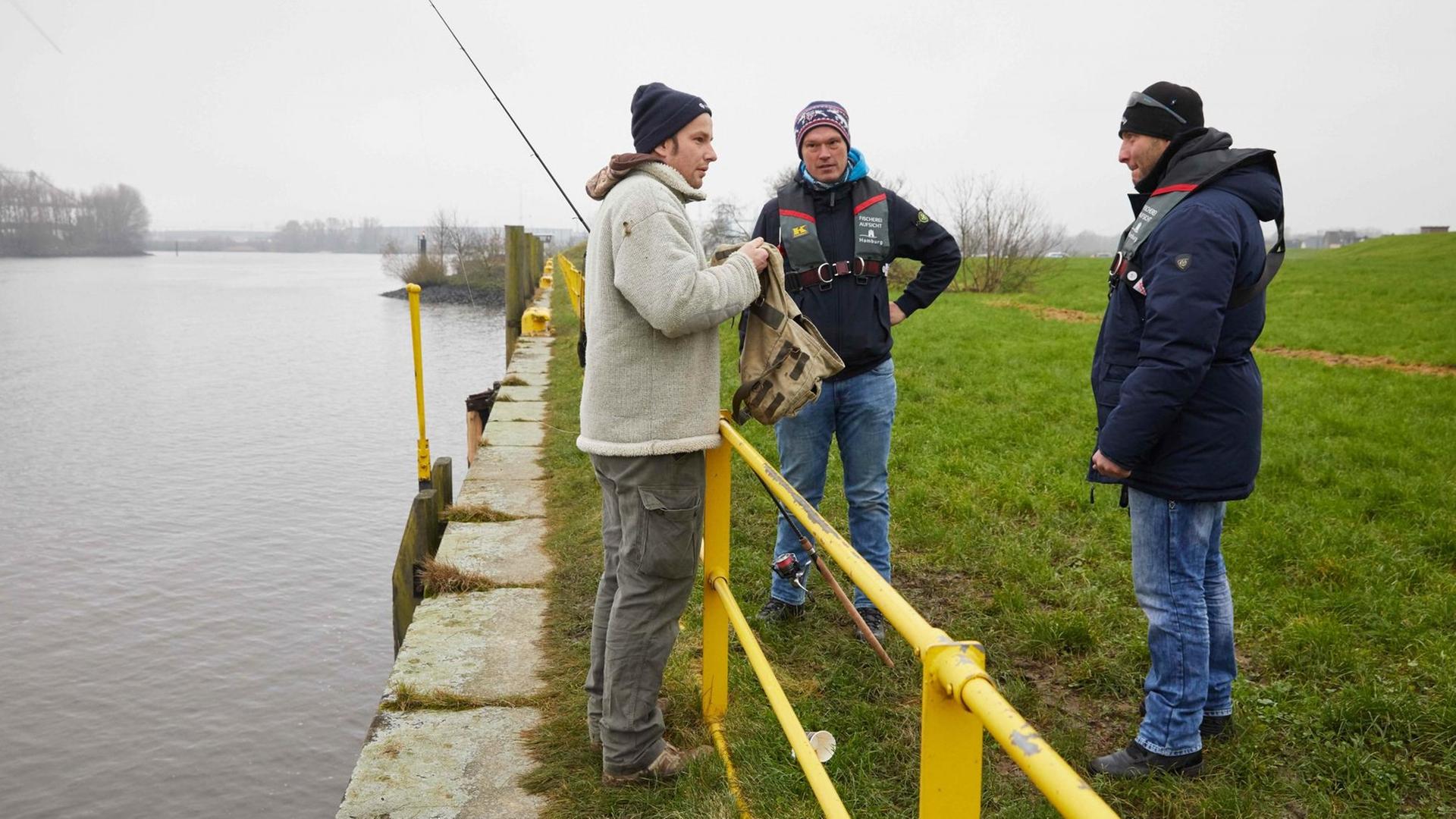 Martin Liebetanz-Vahldiek von der Fischereibehörde (M) und Fischereiaufseher Engin Yurtcan (r) überprüfen in Hamburg im Hafen einen Angler.