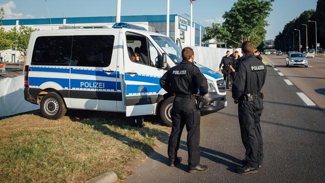Polizisten bewachen am 23.08.2015 die Einfahrt zum Parkplatz vor dem ehemaligen Praktiker-Baumarkt in Heidenau (Sachsen), wo jetzt Flüchtlinge untergebracht werden