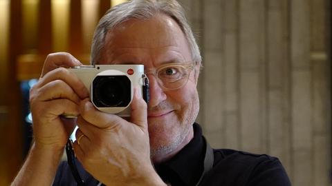 Der Schweizer Autor und Werbefachmann Frank Baumann posiert mit einer Kamera, die er sich vor das rechte Auge hält.