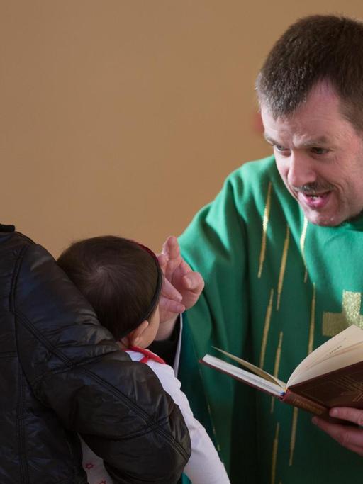 Pastor Gottfried Martens segnet das kleine Mädchen Meliza auf dem Arm ihres Vaters vor ihrer Taufe.