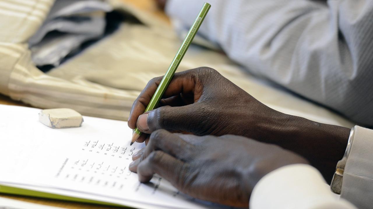 Ein Schüler schreibt beim Deutschunterricht für Asylbewerber auf ein Arbeitsblatt.
