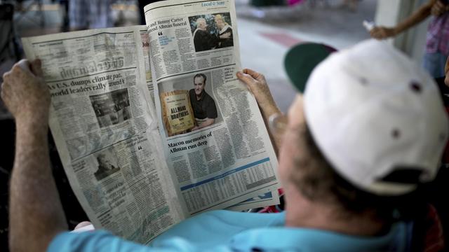 Eine Person mit einer Schirmmütze auf dem Kopf liest eine englischsprachige Zeitung.