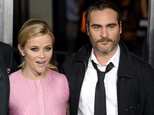 Reese Witherspoon in einem rosa Kleid und Joaquin Phoenix im Anzug, nebeneinander stehend, bis zur Taille sichtbar bei der Premiere von "Inherent Vice" am 10. Dezember 2014 in Los Angeles.