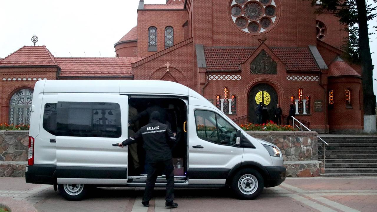 Ein vermummter Polizist steht vor einem Minivan, in dem Teilnehmern der Kundgebung vor der Kirche des hl. Stefans und der hl. Helena in Minsk festgesetzt wurden

