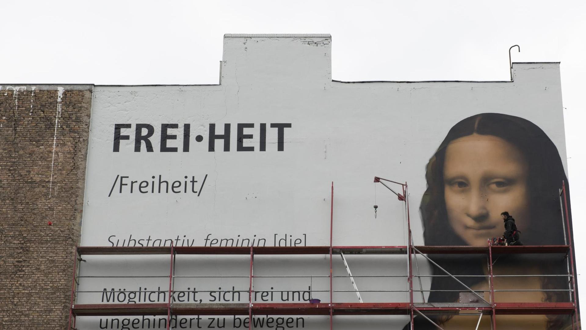 Ein Großtransparent mit dem Konterfei von Mona Lisa und der Aufschrift "Freiheit" ist an einer Häuserwand angebracht. Dazu ist ein Gerüst zu sehen. Ein Großtransparent mit dem Konterfei von Mona Lisa und der Aufschrift "Freiheit" ist an einer Häuserwand angebracht. Dazu ist ein Gerüst zu sehen.