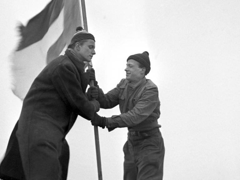 Ein Schwarz-Weiß-Bild zeigt die beiden Studenten Georg von Hatzfeld (l) und Rene Leudesdorff 1951 beim Hissen der Europafahne auf einem F-else der Nordseeinsel Helgoland