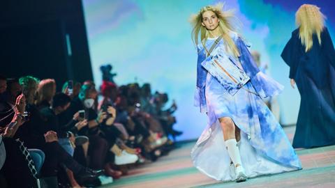 Ein blondes Model in einem extravagant gestalteten, hellblauen Kleid auf einem Laufsteg.