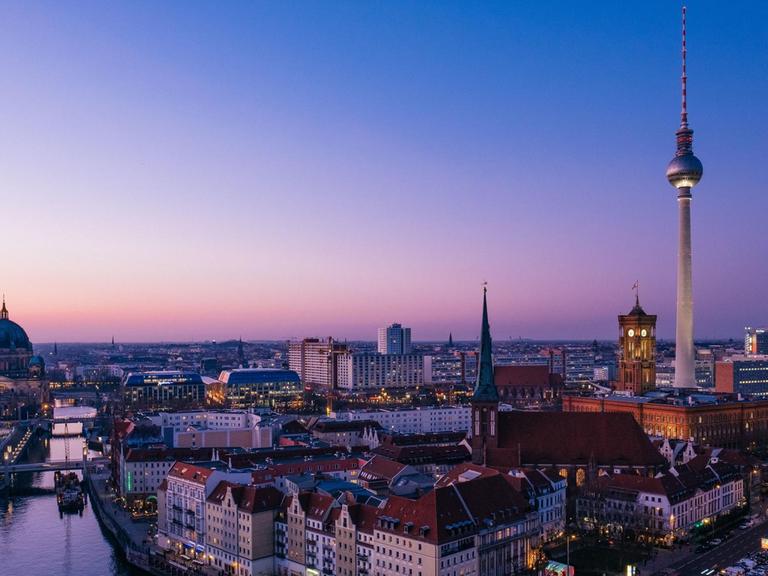 Zu sehen sind die Spree, das Nikolaiviertel mit Nikolaikirche, der Alexanderplatz mit Fernsehturm, Rotes Rathaus und das Park Inn Hotel in der Abenddämmerung.