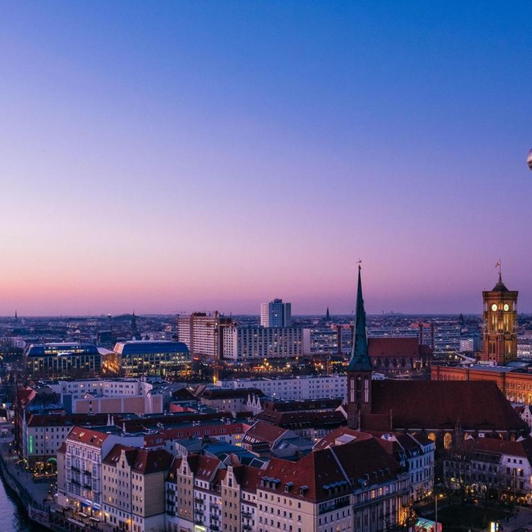 Zu sehen sind die Spree, das Nikolaiviertel mit Nikolaikirche, der Alexanderplatz mit Fernsehturm, Rotes Rathaus und das Park Inn Hotel in der Abenddämmerung.
