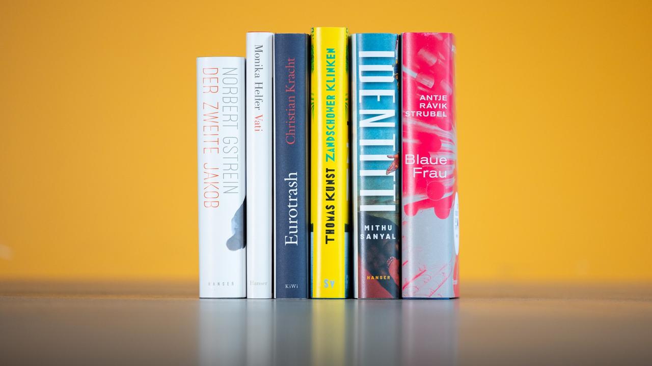 Vor einem gelben Hintergrund stehen 6 Bücher aufgereiht Vor einem gelben Hintergrund stehen 6 Bücher aufgereiht