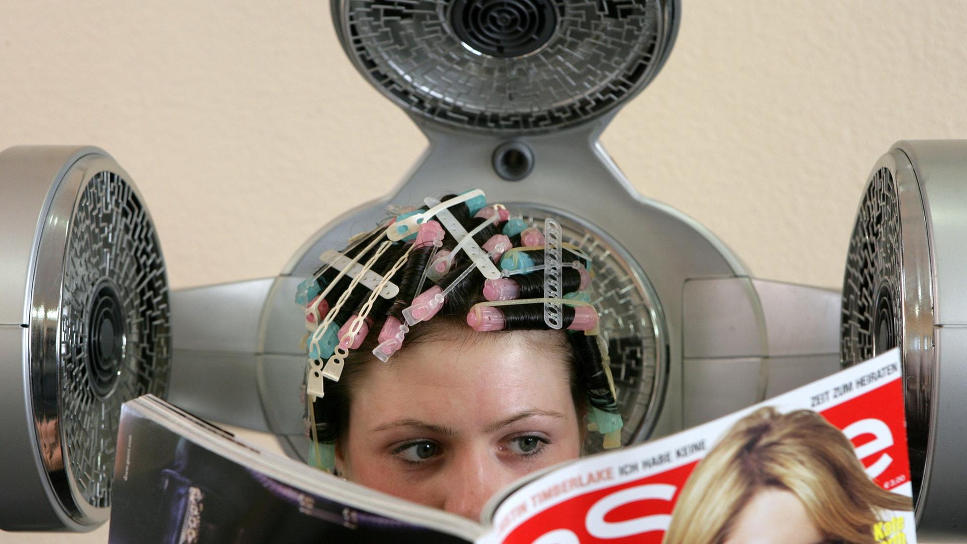 In einem Frisörsalon in Frankfurt (Oder) sitzt eine Frau mit Dauerwellenstäben im Haar unter einem Haubentrockner, aufgenommen am Montag (18.09.2006).