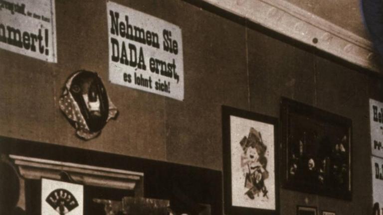 Eröffnung der 1. Internationalen Dada-Messe, Berlin, Buchhandlung Dr. Burchard, 5. Juli 1920 (v. li. stehend Raoul Hausmann, Otto Burchard, Baader, Wieland und Margarete Herzfelde, George Grosz, John Heartfield; sitzend Hannah Höch und Otto Schmalhausen. Foto, spätere Kolorierung.