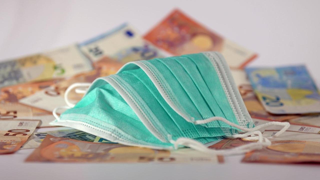 Mundschutz liegt auf Euro-Banknoten. Mundschutz liegt auf Euro-Banknoten.