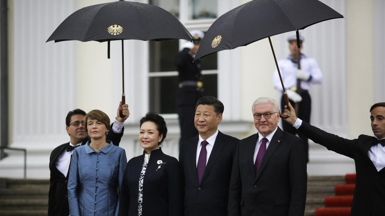Xi Jinping und seine Frau stehen bei ihrer Ankunft am Schloss Bellevue unter Regenschirmen