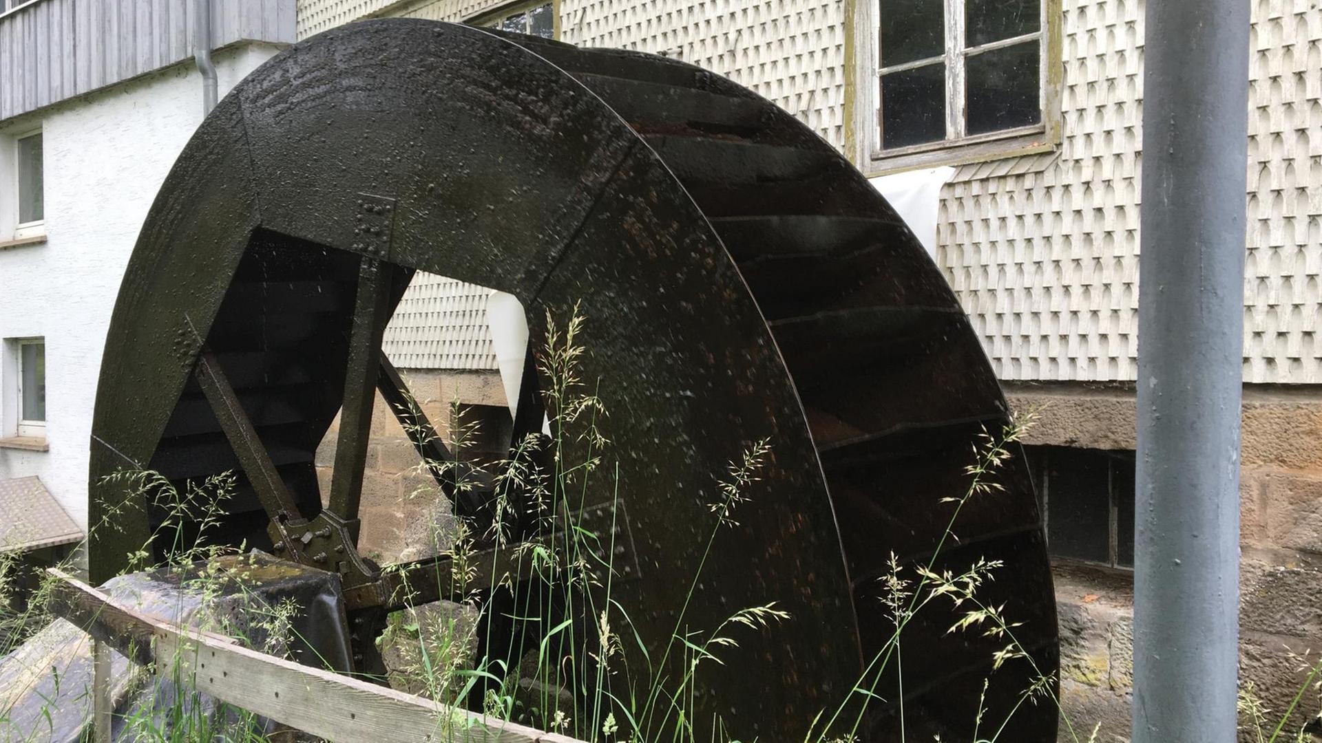 Das metallene Wasserschöpfrad der Kappmühle im Dorf Mackenzell in der hessischen Rhön vor dem Gebäude der Mühle Das metallene Wasserschöpfrad der Kappmühle im Dorf Mackenzell in der hessischen Rhön vor dem Gebäude der Mühle
