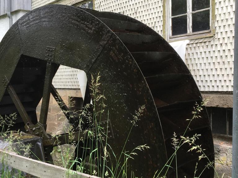 Das metallene Wasserschöpfrad der Kappmühle im Dorf Mackenzell in der hessischen Rhön vor dem Gebäude der Mühle