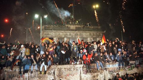 Ausgelassen feiern Menschen am 31.12.1989 auf der Berliner Mauer vor dem Brandenburger Tor.