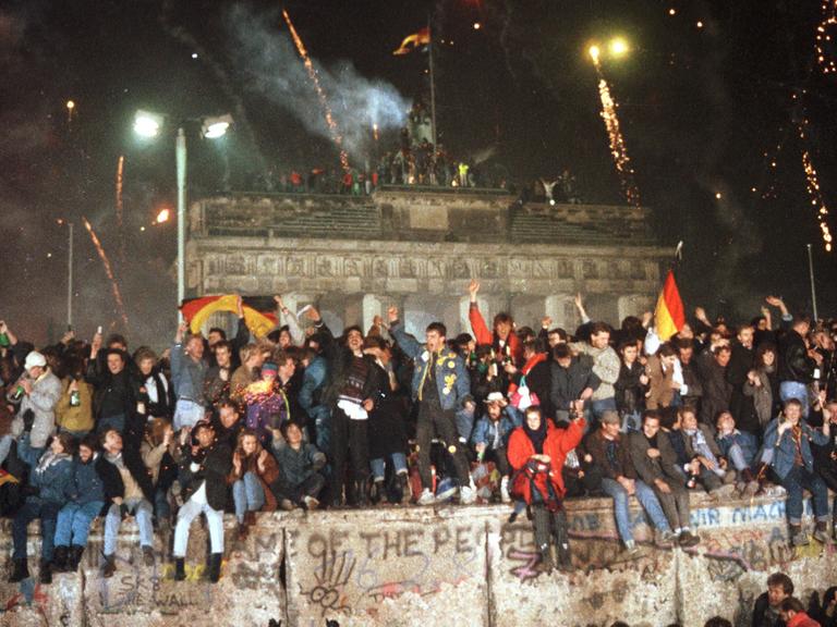 Ausgelassen feiern Menschen am 31.12.1989 auf der Berliner Mauer vor dem Brandenburger Tor.